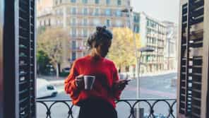 Chica tomando café y mirando el móvil en el balcón