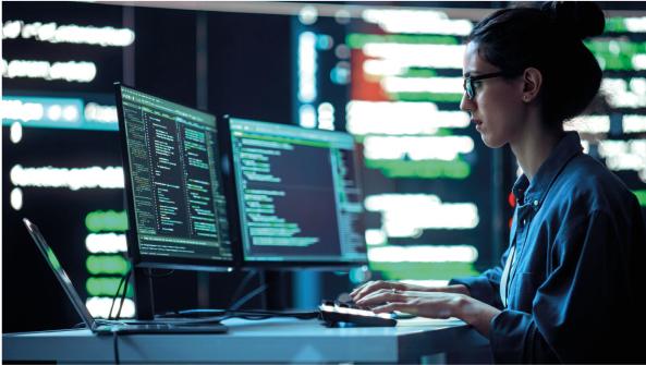 una persona trabajando en Ciberseguridad con 2 pantallas de ordenador y datos