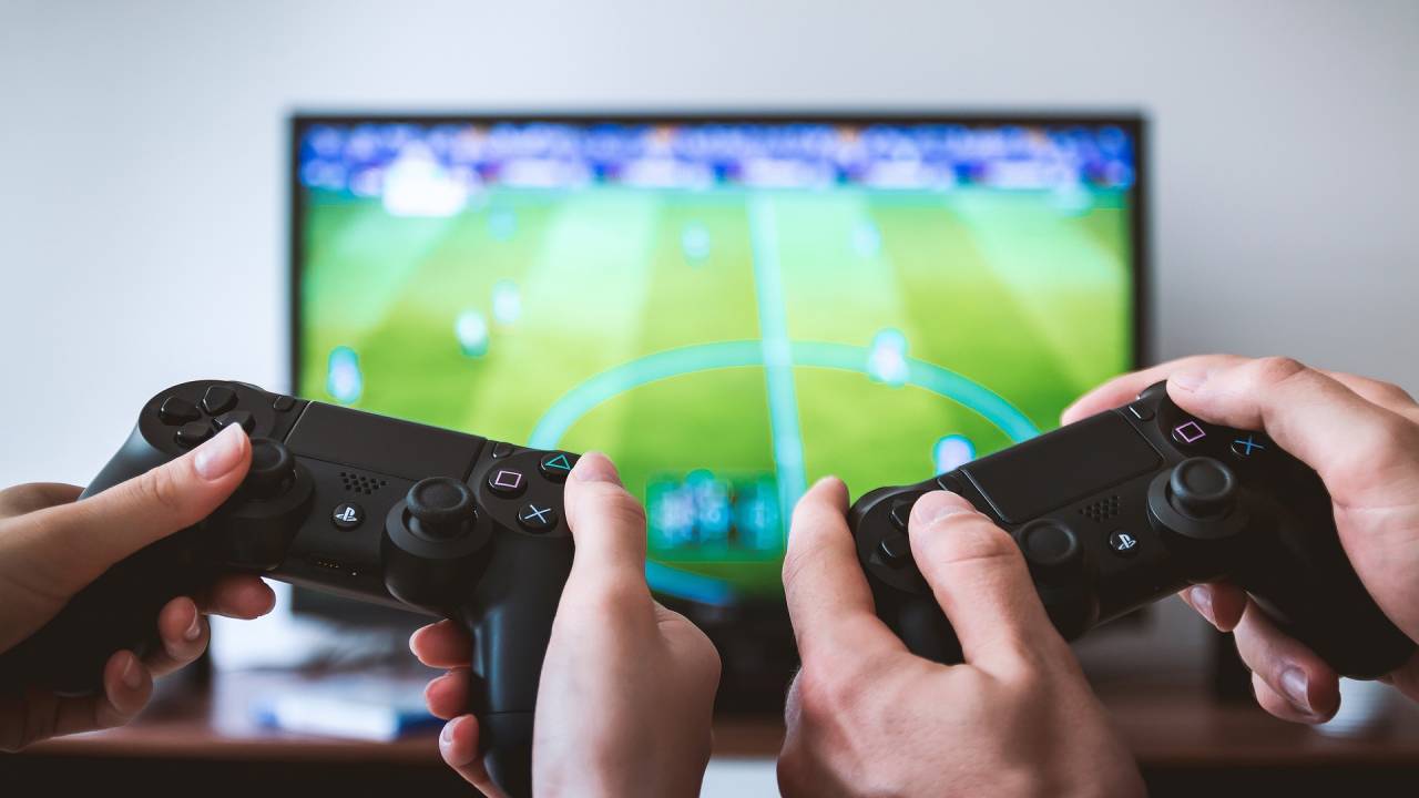 manos agarrando mandos de videoconsola con una tele de fondo