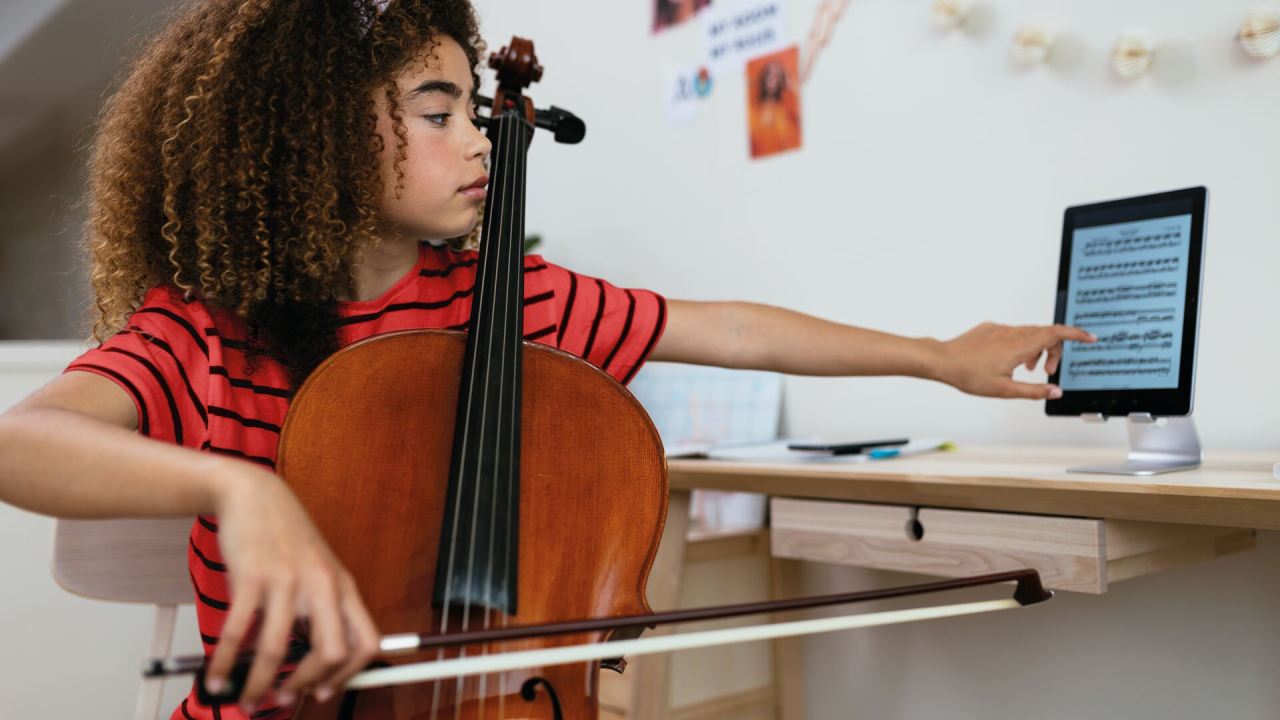 una niña tocando el violín mientras ve la partitura en una tablet